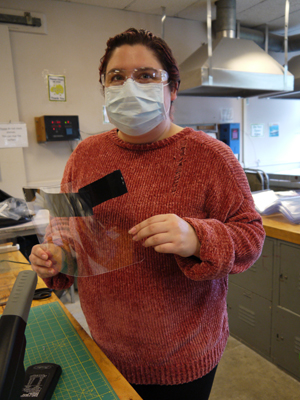 Student wearing a face mask holding a face shield in progress