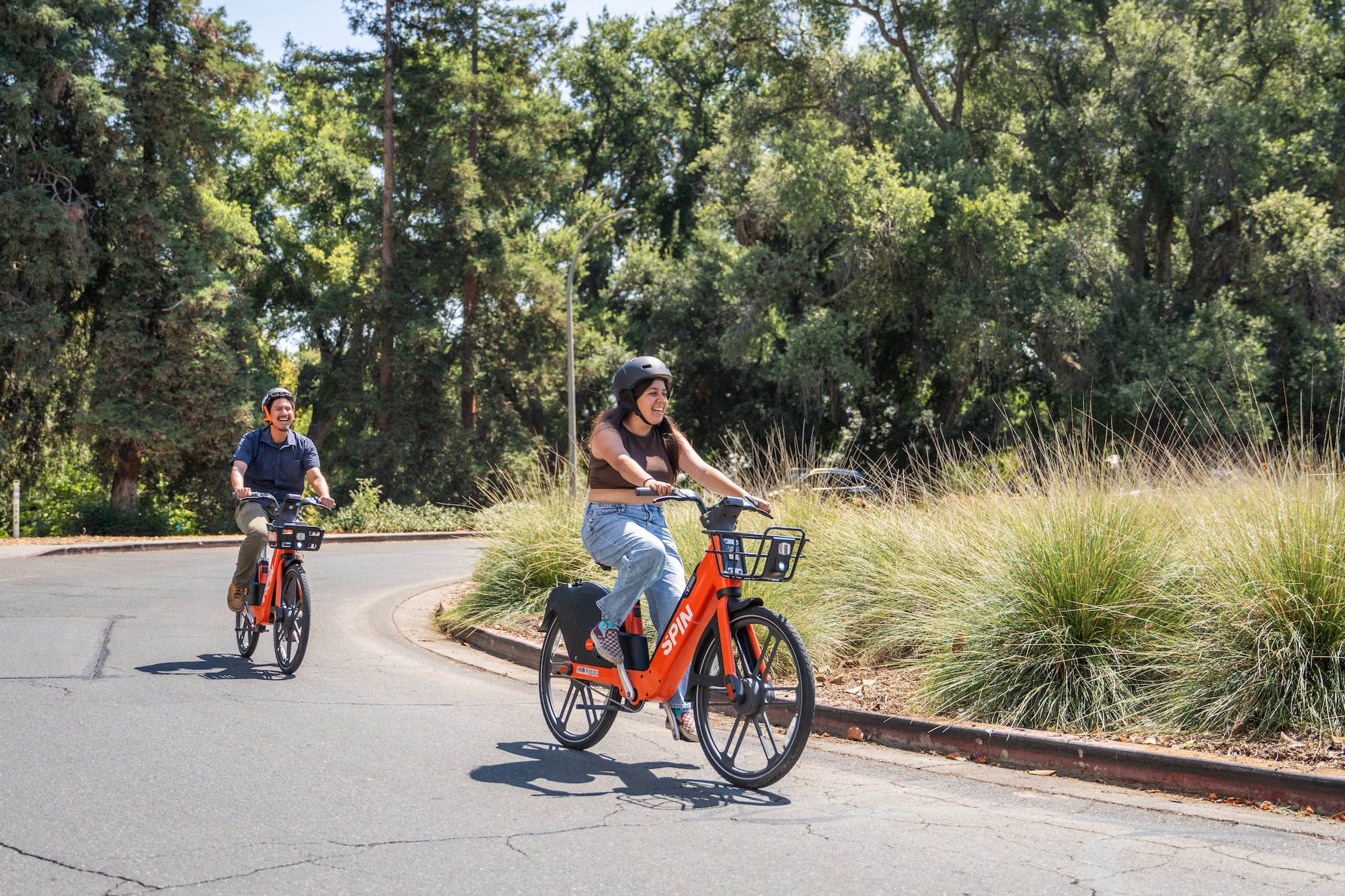 Two people ride Spin e-bikes on campus