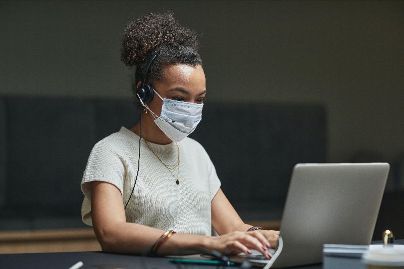 Person working at a computer, wearing a face covering