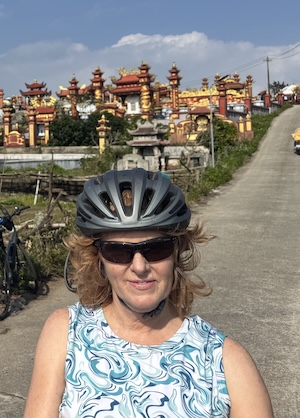 Clare Shinnerl smiles, wearing a bike help standing in front of red and gold structures