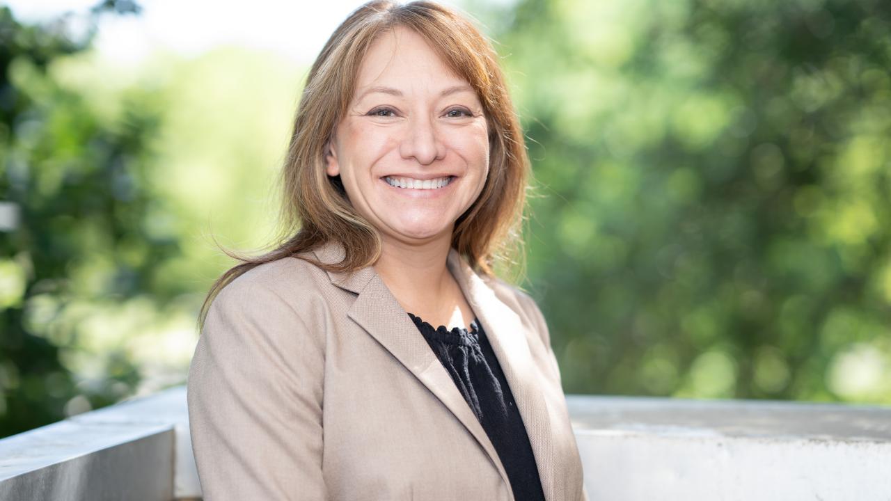 Smiling middle-aged woman in beige blazer outdoors, blurred green background, photo