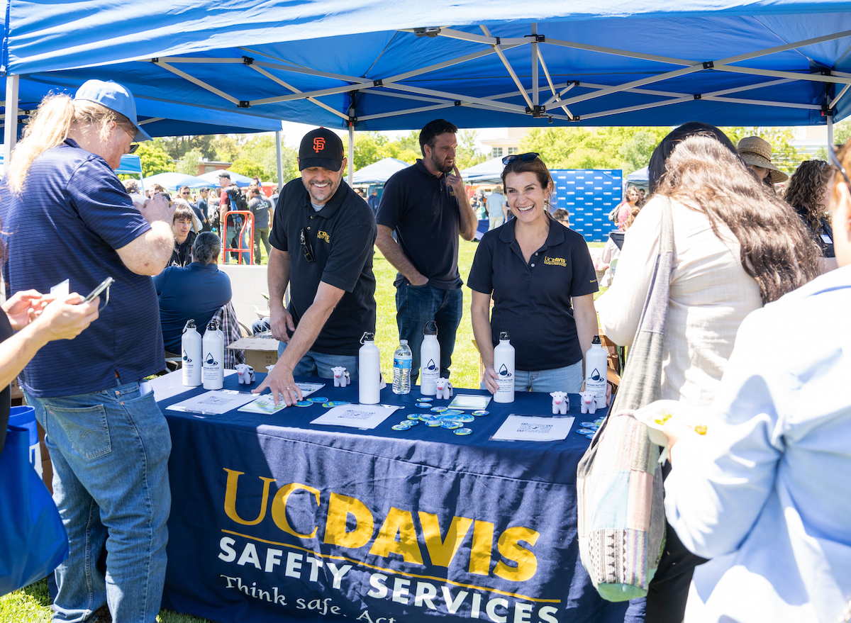 Safety Services staff members smile at their booth while people line up at the 2023 Thank Goodness for Staff Picnic