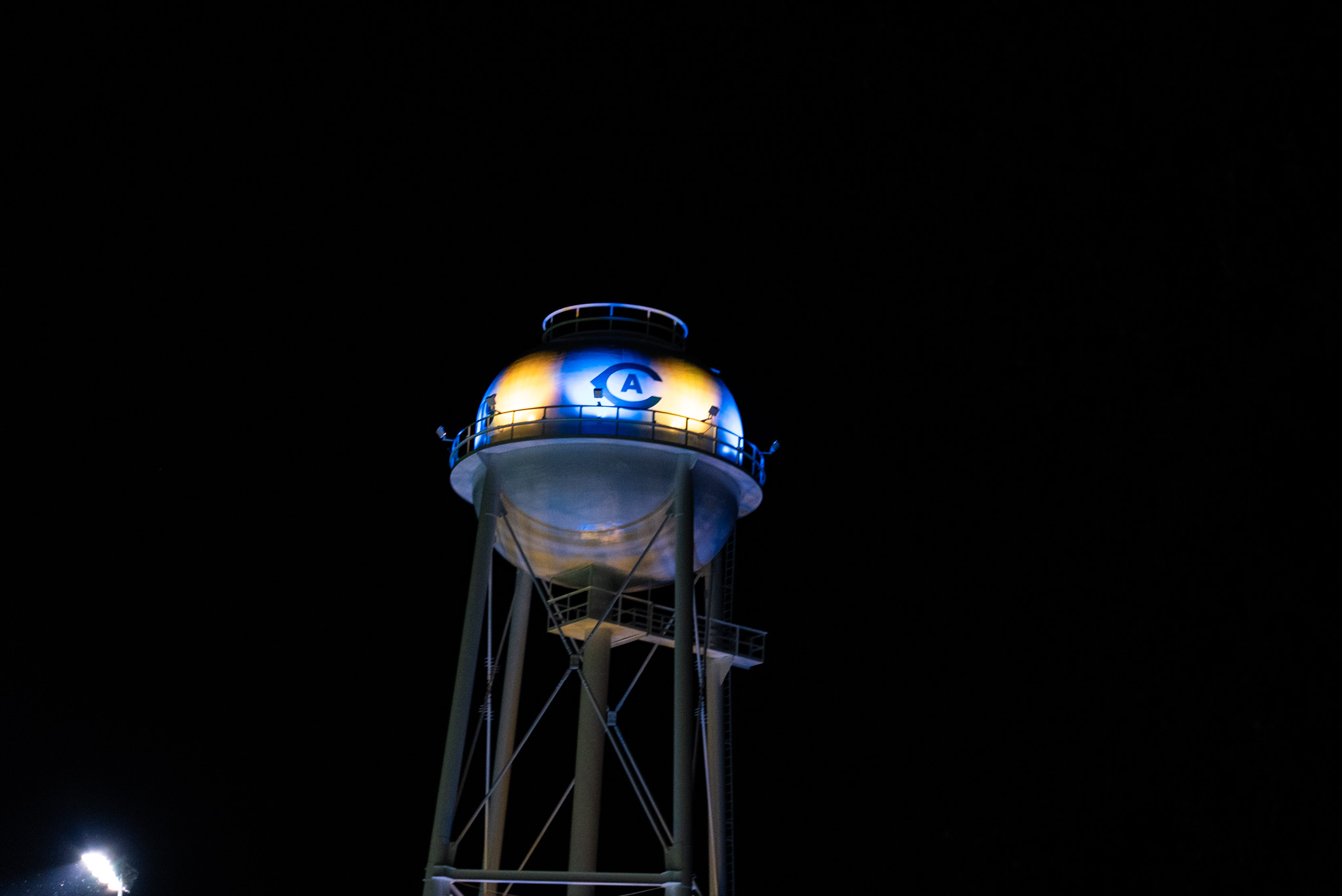 Blue and yellow lights illuminate the UC Davis athletics logo on a water tower on the UC Davis campus