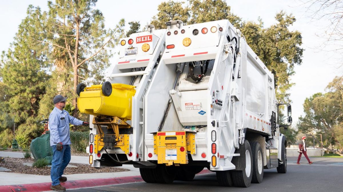 A custodial services employee stands by as the new compost truck collects a compost bin