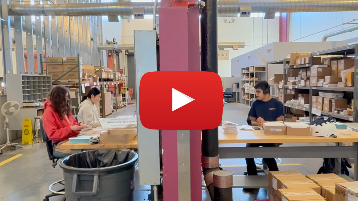 Three students work at desks among packages
