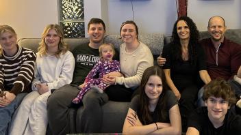 A group of nine people of various ages sit together on a couch.