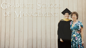 Graduate Kelly Ratliff and mom smiling in front of UC Davis Graduate School of Management sign