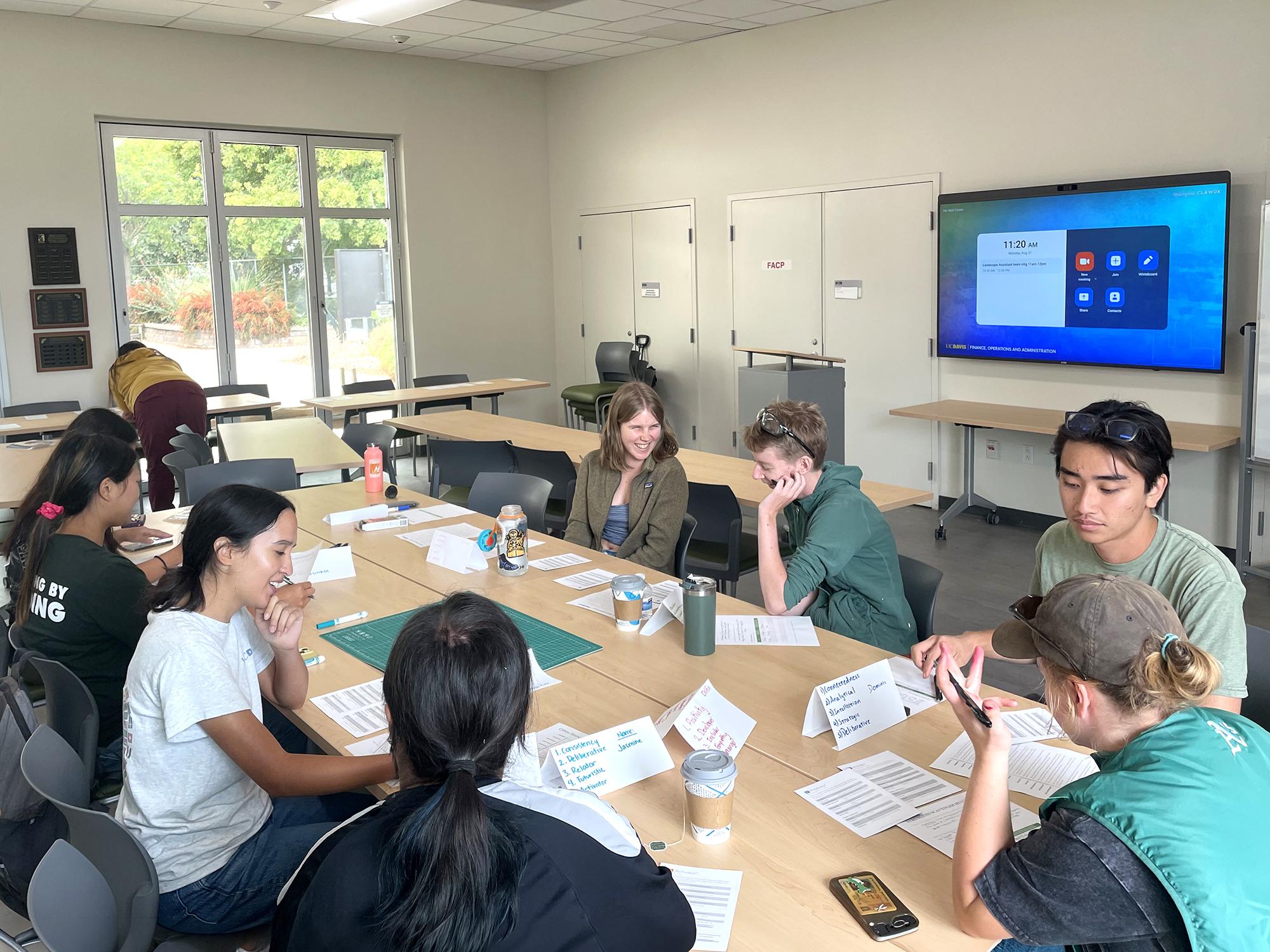 Group of students seated around table in a bright classroom.