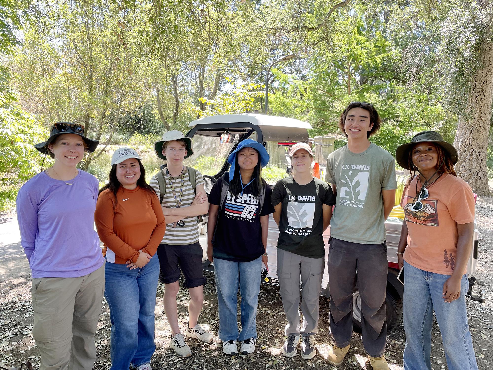 Group photo of 7 diverse students standing under a tree.