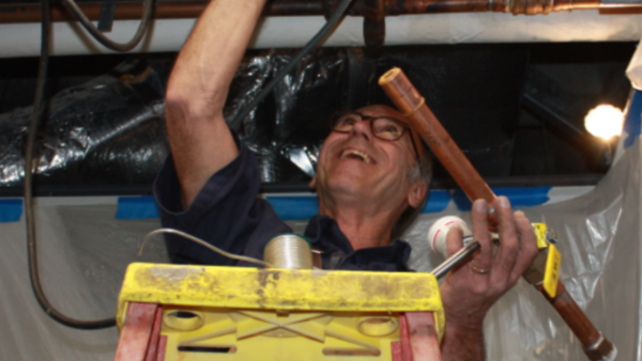 Plumber Chuck Peters installing a new valve and section of pipe. Photo of employee working with water pipes.