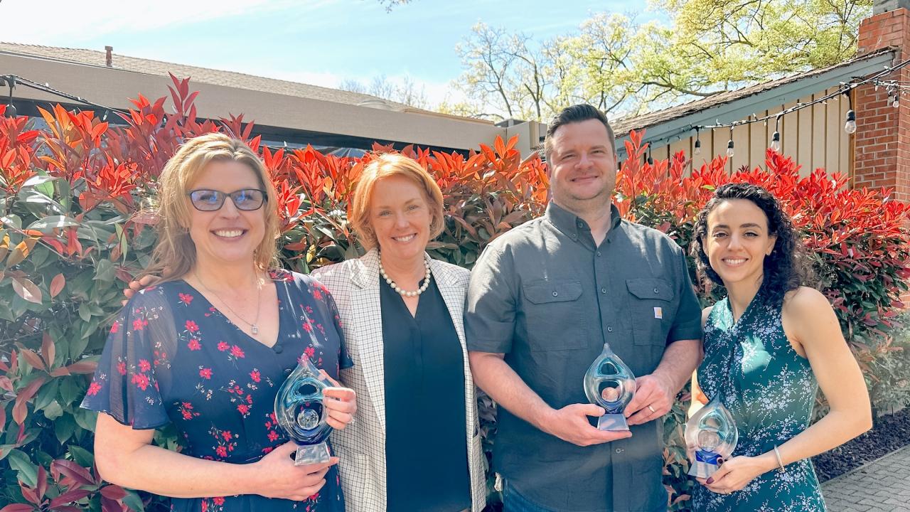 Jennifer Thompson, Aaron Knapek, and Amber Sharpe stand holding awards, posing with Clare Shinnerl