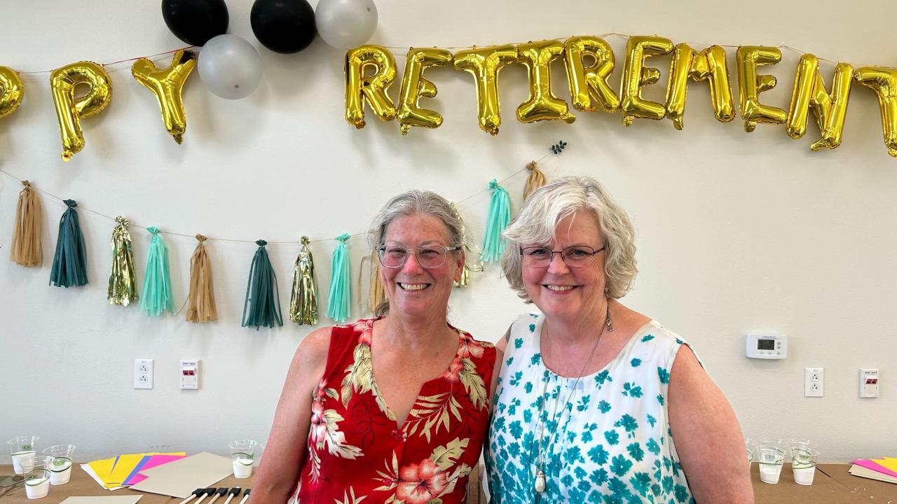 Mary Gibson and Roxanne Loe smiling at their retirement party, with decorations in the background