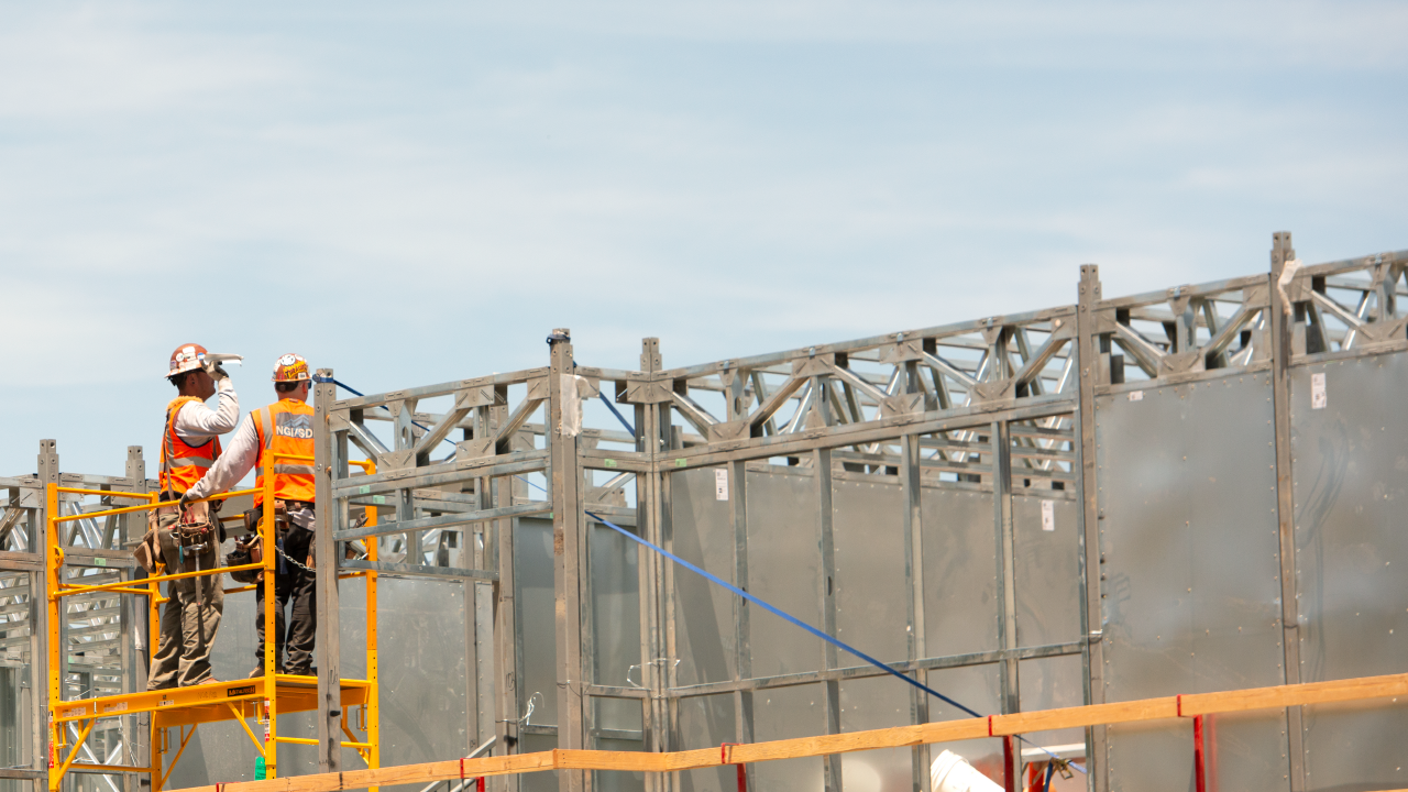 Two construction workers looking at the top of building frame.