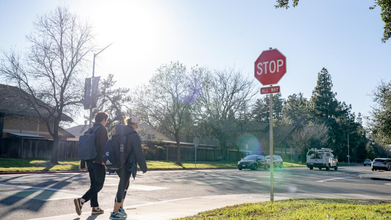 walkers on a crosswalk approach a stop sign with vehicles nearby 