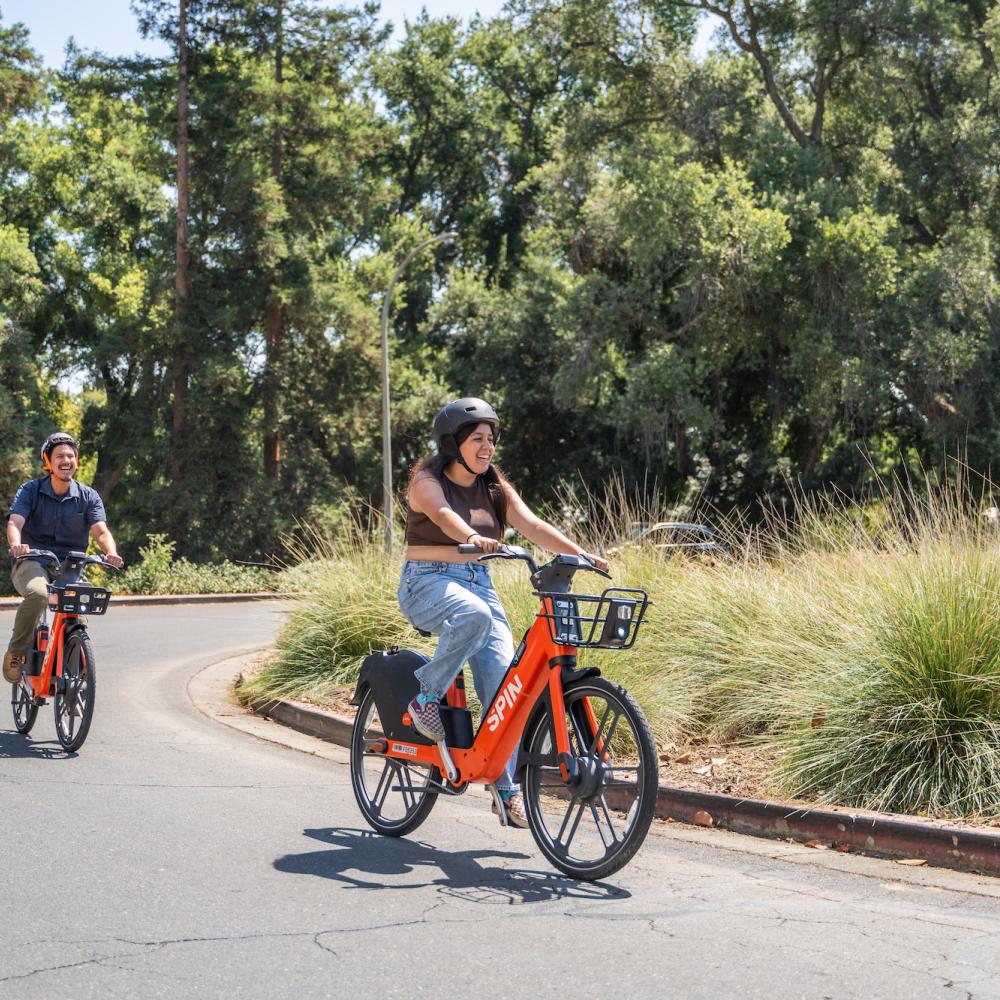 Two people ride Spin e-bikes on campus