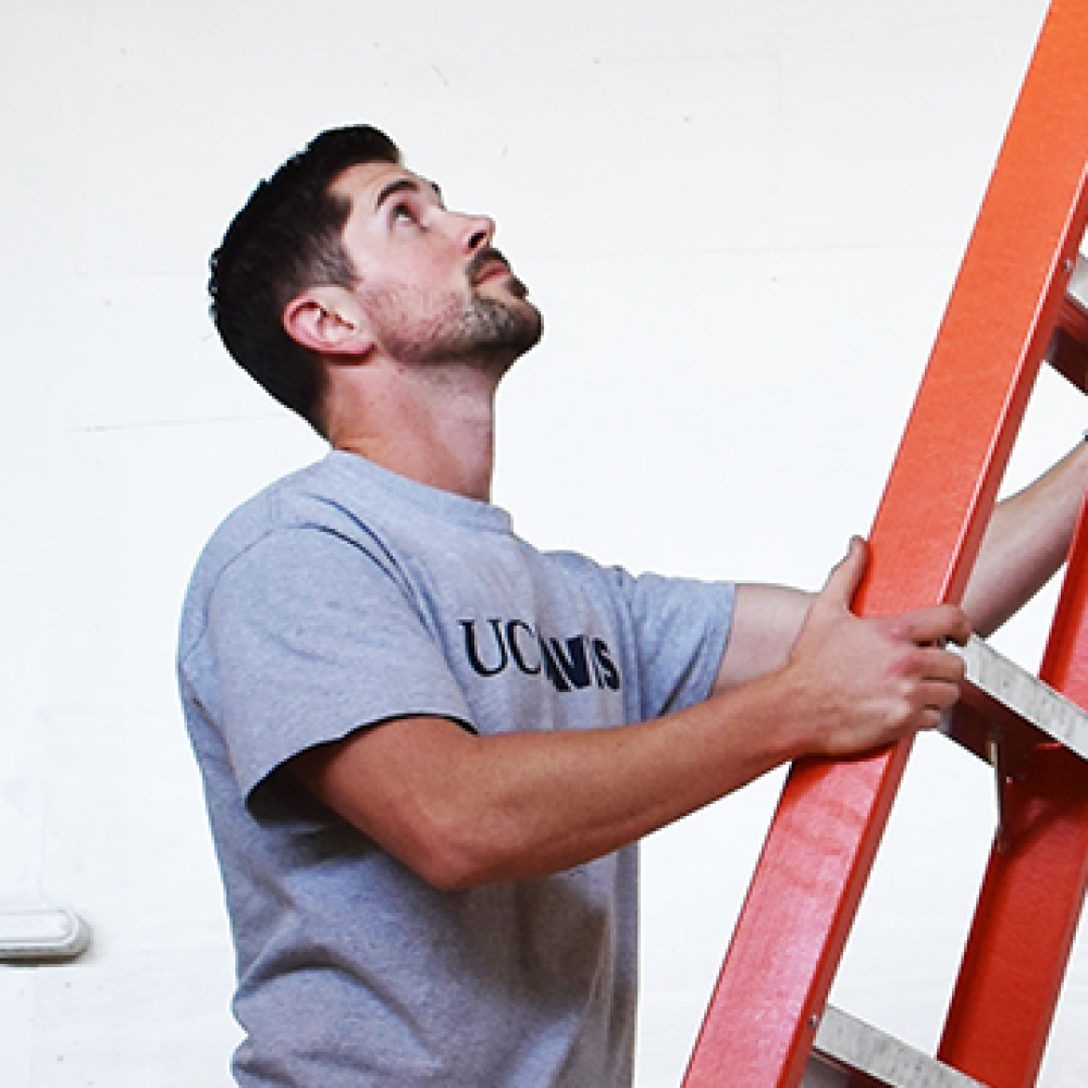 Facilities employee standing on a ladder