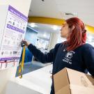 An EMT in a UC Davis shirt with a box of supplies, unlocks the Narcan cabinet in the Memorial Union